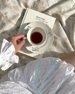 Minimalist lifestyle UGC photography featuring a coffee cup on a book by Adrian Frutiger, with white lace fabric and warm sunlight.